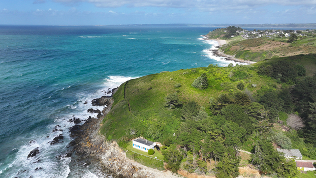 Aerial view of the rugged coastline with a white house on a green cliff overlooking the turquoise sea and crashing waves Locquirec Brittany France. Aerial view of the rugged coastline with a white house on a green cliff overlooking the turquoise sea and crashing waves Locquirec Brittany France.