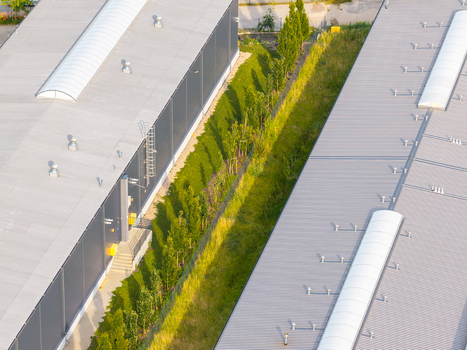 Aerial view of industrial buildings with metal roofs and skylights separated by a narrow strip of green grass and trees in Kowale Pomeranian Voivodeship Poland. Aerial view of industrial buildings with metal roofs and skylights separated by a narrow strip of green grass and trees in Kowale Pomeranian Voivodeship Poland.