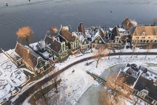 Aerial view of Zaanse Schans featuring traditional green wooden houses covered in snow along the Zaan river in Zaandam Noord Holland Netherlands. Aerial view of Zaanse Schans featuring traditional green wooden houses covered in snow along the Zaan river in Zaandam Noord Holland Netherlands.