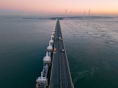 Aerial view of the Oosterscheldekering storm surge barrier with wind turbines and a road at sunset Zeeland Netherlands.