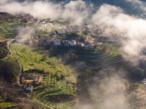 Aerial view of Avo village with terraced green fields and white houses partially covered by morning mist in Oliveira do Hospital Coimbra District Portugal.