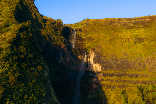 Aerial view of Poco da Ribeira do Ferreiro waterfall cascading down lush green cliffs under a clear blue sky in Fajazinha Azores Portugal. Aerial view of Poco da Ribeira do Ferreiro waterfall cascading down lush green cliffs under a clear blue sky in Fajazinha Azores Portugal.