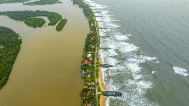 Aerial view of Mattu Beach a narrow strip of land separating the backwaters from the Arabian Sea with palm trees coastal houses and stone breakwaters in Udupi Karnataka India.