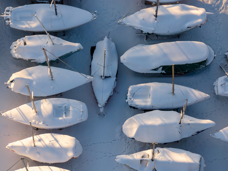Aerial view of snow covered sailboats parked on land during winter with golden sunlight and footprints in the snow in Trakai Vilnius County Lithuania. Aerial view of snow covered sailboats parked on land during winter with golden sunlight and footprints in the snow in Trakai Vilnius County Lithuania.