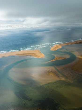 Aerial view of the winding estuary where the river meets the sea under a sky heavy with clouds Rauðisandur Vesturbyggð Iceland. Aerial view of the winding estuary where the river meets the sea under a sky heavy with clouds Rauðisandur Vesturbyggð Iceland.