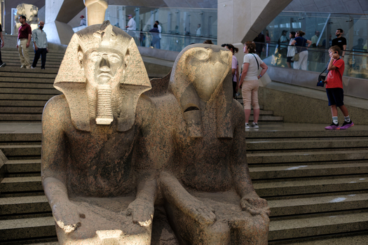 Giza Egypt 16 May 2026 View of ancient granite statues of King Ramses II and a deity on the grand staircase inside the Grand Egyptian Museum with visitors in the background.