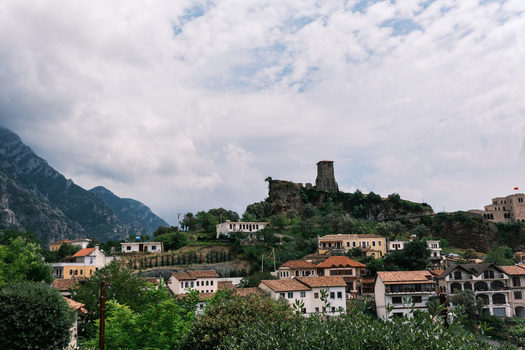 View of the historic Kruje Castle and traditional houses with red tiled roofs nestled against rugged mountains under a cloudy sky in Kruje Durres County Albania.