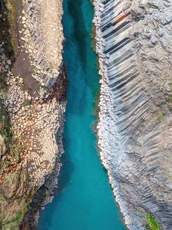 Aerial view of Studlagil Canyon featuring dramatic basalt columns lining the turquoise river in Iceland. Aerial view of Studlagil Canyon featuring dramatic basalt columns lining the turquoise river in Iceland.