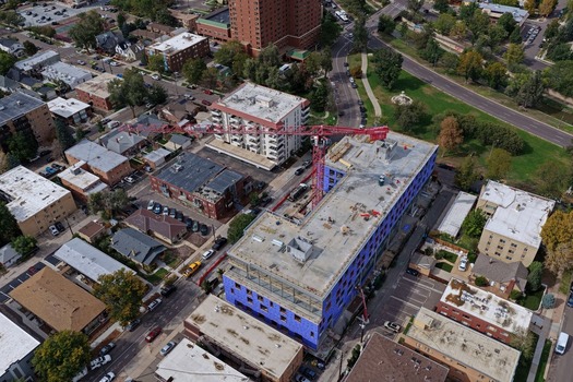 Aerial view of a construction site with a red tower crane over a building wrapped in blue protective material surrounded by urban residential buildings in Denver Colorado United States. Aerial view of a construction site with a red tower crane over a building wrapped in blue protective material surrounded by urban residential buildings in Denver Colorado United States.
