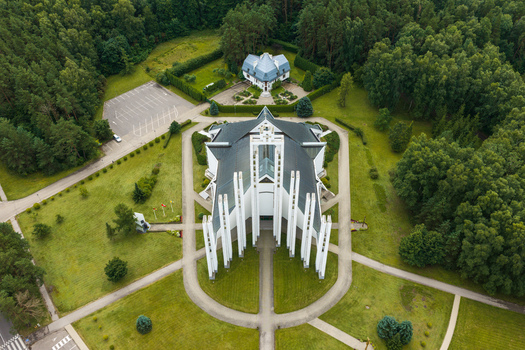 Aerial view of the modern Elektrenai Church of the Virgin Mary Queen of Martyrs with white pillars and dark roof surrounded by forest and pathways in Elektrenai Vilnius County Lithuania. Aerial view of the modern Elektrenai Church of the Virgin Mary Queen of Martyrs with white pillars and dark roof surrounded by forest and pathways in Elektrenai Vilnius County Lithuania.