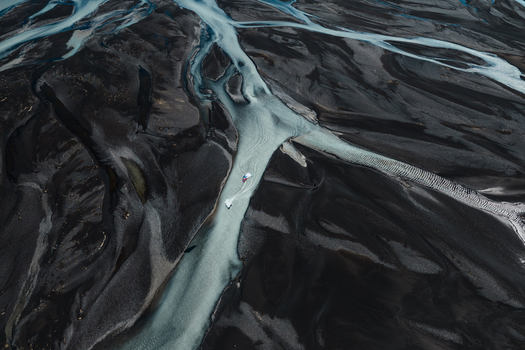 Aerial view of a small boat navigating the glacial river channels winding through the dark volcanic sand plains of Skaftarhreppur Iceland.