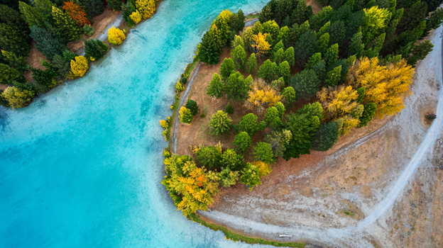 Aerial view of a turquoise river winding past a peninsula covered in vibrant autumn trees with yellow and green foliage Twizel Canterbury Region New Zealand.