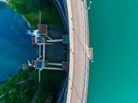 Aerial view of the Barrage de Rossens dam with a curved road separating turquoise waters from lush forest in Pont la Ville Fribourg Switzerland.