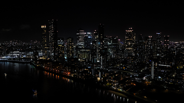 Aerial view of the illuminated Canary Wharf skyline at night with skyscrapers reflecting on the River Thames in London England United Kingdom. Aerial view of the illuminated Canary Wharf skyline at night with skyscrapers reflecting on the River Thames in London England United Kingdom.