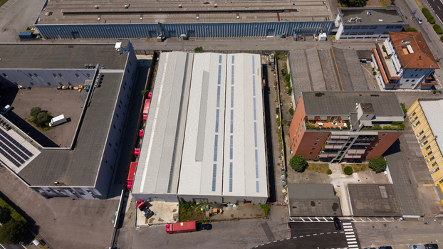 Aerial view of an industrial warehouse with a metal roof adjacent to a brick residential building parking areas and urban infrastructure in Milan Lombardy Italy. Aerial view of an industrial warehouse with a metal roof adjacent to a brick residential building parking areas and urban infrastructure in Milan Lombardy Italy.
