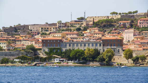 View of the town rising from the azure sea terracotta roofs and warm stone buildings contrasting with the vibrant blue water Portoferraio Elba Tuscany Italy. View of the town rising from the azure sea terracotta roofs and warm stone buildings contrasting with the vibrant blue water Portoferraio Elba Tuscany Italy.