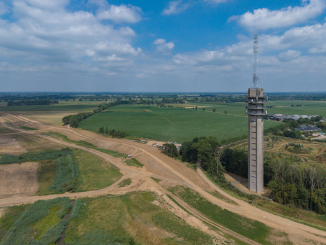 Aerial view of a tall communications tower standing in a rural landscape with green fields and dirt roads under a blue sky in the Netherlands. Aerial view of a tall communications tower standing in a rural landscape with green fields and dirt roads under a blue sky in the Netherlands.