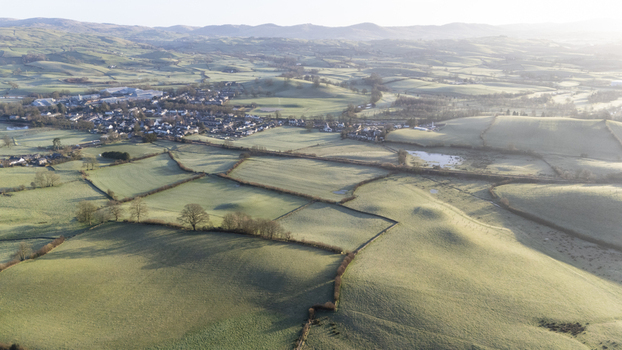 Aerial view of rolling green hills meet a quaint village nestled in the valley with a soft hazy light bathing the landscape Kirkby Lonsdale England United Kingdom. Aerial view of rolling green hills meet a quaint village nestled in the valley with a soft hazy light bathing the landscape Kirkby Lonsdale England United Kingdom.