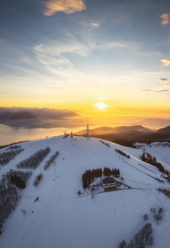 Aerial view of Mottarone ski resort covered in snow during a golden sunrise with mountain peaks and Lake Maggiore in the background in Mottarone Piedmont Italy. Aerial view of Mottarone ski resort covered in snow during a golden sunrise with mountain peaks and Lake Maggiore in the background in Mottarone Piedmont Italy.