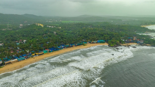 Aerial view of Palolem Beach with lush green palm trees sandy shore and waves crashing on the coastline in Canacona Goa India.