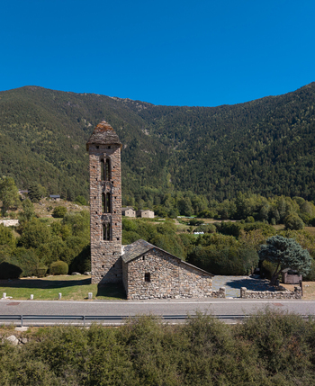Aerial view of the Romanesque church of Sant Miquel Engolasters with its stone bell tower surrounded by trees and mountains under a clear blue sky in Engolasters Escaldes Engordany Andorra. Aerial view of the Romanesque church of Sant Miquel Engolasters with its stone bell tower surrounded by trees and mountains under a clear blue sky in Engolasters Escaldes Engordany Andorra.