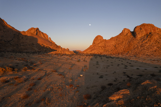 Aerial view of rugged sun kissed peaks and valleys cast long shadows over the arid landscape a solitary vehicle traversing the dusty terrain Spitzkoppe Namibia. Aerial view of rugged sun kissed peaks and valleys cast long shadows over the arid landscape a solitary vehicle traversing the dusty terrain Spitzkoppe Namibia.