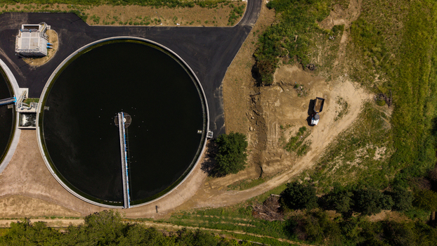 Aerial view of a wastewater treatment plant with large circular sedimentation tanks and a construction vehicle on a dirt path in Milan Lombardy Italy. Aerial view of a wastewater treatment plant with large circular sedimentation tanks and a construction vehicle on a dirt path in Milan Lombardy Italy.