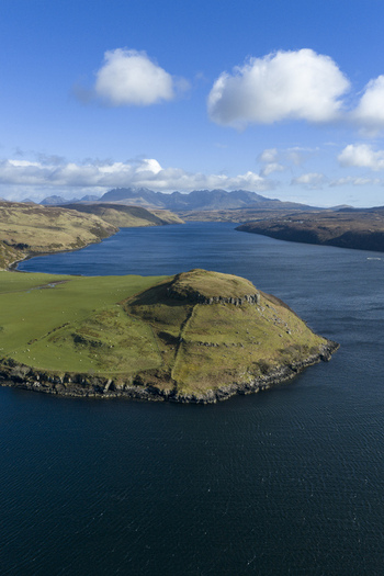 Aerial view of the green hills and rocky coastline of Gesto Bay Viewpoint overlooking the blue waters of Loch Harport under a bright sky Isle of Skye Scotland United Kingdom.
