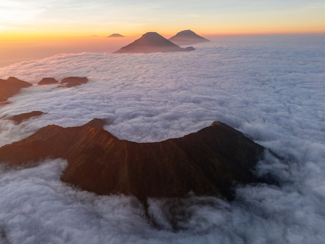 Aerial view of the volcanic landscape of Mount Bismo rising above a thick sea of clouds during a golden sunrise in Kecamatan Kejajar Jawa Tengah Indonesia.