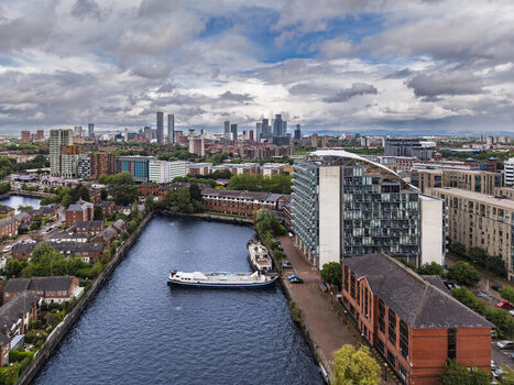 Aerial view of MediaCityUK featuring modern architecture the Manchester Ship Canal and a canal boat with the Salford skyline under a cloudy sky in Salford England United Kingdom. Aerial view of MediaCityUK featuring modern architecture the Manchester Ship Canal and a canal boat with the Salford skyline under a cloudy sky in Salford England United Kingdom.