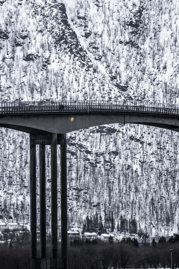 View of the Tromso Bridge with people walking along the path against a backdrop of snow covered mountains in Tromso Troms Norway. View of the Tromso Bridge with people walking along the path against a backdrop of snow covered mountains in Tromso Troms Norway.