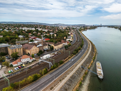 Aerial view of the Danube riverfront in Budapest Hungary with a barge riverside road traffic railway tracks industrial buildings and dense urban neighborhoods.