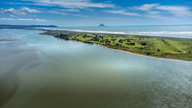 Aerial view of the Ohope spit featuring a golf course coastal dunes and the Pacific Ocean under a clear blue sky in Ohope Bay of Plenty Region New Zealand.
