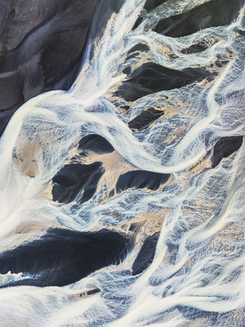 Aerial view of a complex braided glacial river system with white water channels flowing through dark volcanic sand deposits in Iceland. Aerial view of a complex braided glacial river system with white water channels flowing through dark volcanic sand deposits in Iceland.