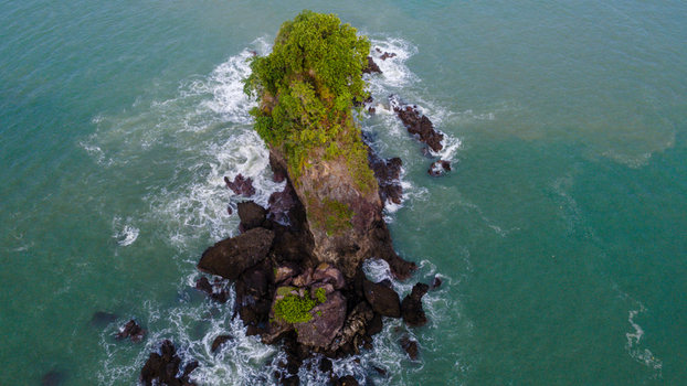 Aerial view of the Karang Agung rock formation with lush green vegetation surrounded by turquoise sea water and crashing waves at Ayah Central Java Indonesia. Aerial view of the Karang Agung rock formation with lush green vegetation surrounded by turquoise sea water and crashing waves at Ayah Central Java Indonesia.