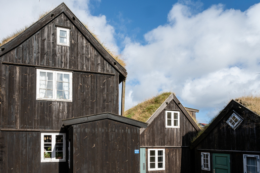 View of traditional black wooden houses with grass roofs and white window frames under a blue sky in the Faroe Islands. View of traditional black wooden houses with grass roofs and white window frames under a blue sky in the Faroe Islands.
