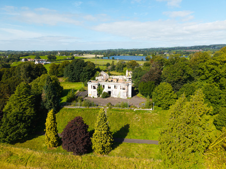 Aerial view of a derelict mansion surrounded by overgrown trees and lush green fields with a lake in the distance in Lisburn Northern Ireland United Kingdom. Aerial view of a derelict mansion surrounded by overgrown trees and lush green fields with a lake in the distance in Lisburn Northern Ireland United Kingdom.