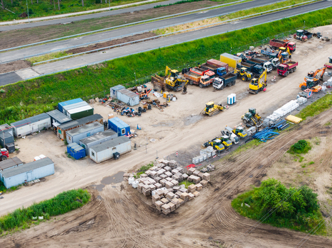 Aerial view of the construction site for Stage 4 of the Southern Bridge project featuring heavy machinery shipping containers and stacks of paving materials in Riga Latvia. Aerial view of the construction site for Stage 4 of the Southern Bridge project featuring heavy machinery shipping containers and stacks of paving materials in Riga Latvia.