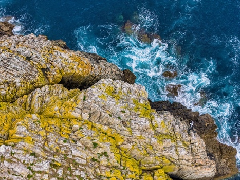 Aerial view of the rugged rocky coastline of Silence Beach Viewpoint with lichen covered cliffs and crashing blue waves in Cudillero Asturias Spain.
