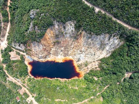 Aerial view of Laghetto delle conche or Lago di Sangue with its deep red water surrounded by rocky cliffs and lush green forest in Rio Marina Toscana Italy.