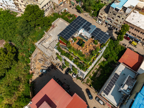 Aerial view of a building featuring a lush rooftop garden with seating areas and solar panels situated in an urban neighborhood in Udaipur Rajasthan India.