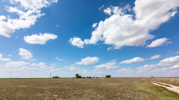 View of a rural landscape with a dirt road stretching through dry fields under a vast blue sky with scattered white clouds in Oklahoma City Oklahoma United States.