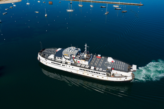 View of a large white ferry boat cruising through the blue waters of Martha s Vineyard with anchored sailboats in the background in Edgartown Massachusetts United States.