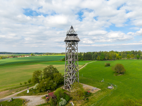 Aerial view of the wooden Bohdanka Lookout Tower surrounded by green fields and trees under a blue sky with clouds in Bohdanec Central Bohemian Region Czechia. Aerial view of the wooden Bohdanka Lookout Tower surrounded by green fields and trees under a blue sky with clouds in Bohdanec Central Bohemian Region Czechia.