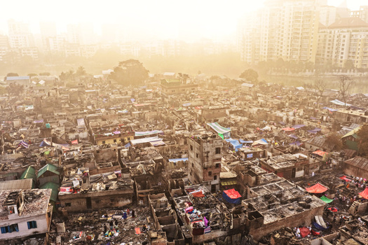 Aerial view of Korail Basti showing dense settlement with charred structures makeshift roofs and narrow alleys under a hazy golden sunset light Dhaka Dhaka Division Bangladesh.