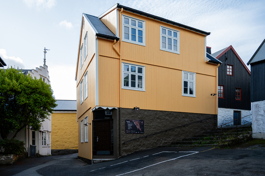 View of a traditional yellow wooden house with a dark stone foundation and white framed windows in the historic Tinganes district Faroe Islands. View of a traditional yellow wooden house with a dark stone foundation and white framed windows in the historic Tinganes district Faroe Islands.