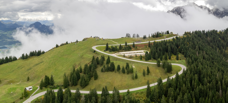 Aerial view of the winding road through the alpine landscape of Berchtesgaden surrounded by lush green meadows and dense pine forests in Berchtesgaden Bavaria Germany.