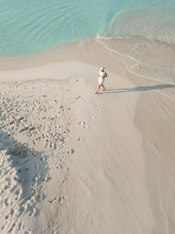 Aerial view of a tranquil beach where turquoise waters meet the pristine white sand with a lone figure strolling along the shore Dhidhdhoo Maldives.