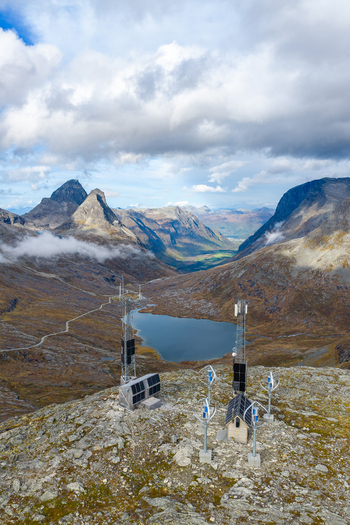 Aerial view of a remote power station with wind turbines and solar panels on a rocky mountain ridge overlooking a lake Andalsnes More og Romsdal Norway.
