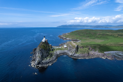 Aerial view of the Sanda Island lighthouse perched on a rocky cliff surrounded by the deep blue sea and green grassy hills in Argyll and Bute Council Scotland United Kingdom.